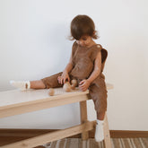 Toddler sitting and playing while wearing brown corduroy baby overalls